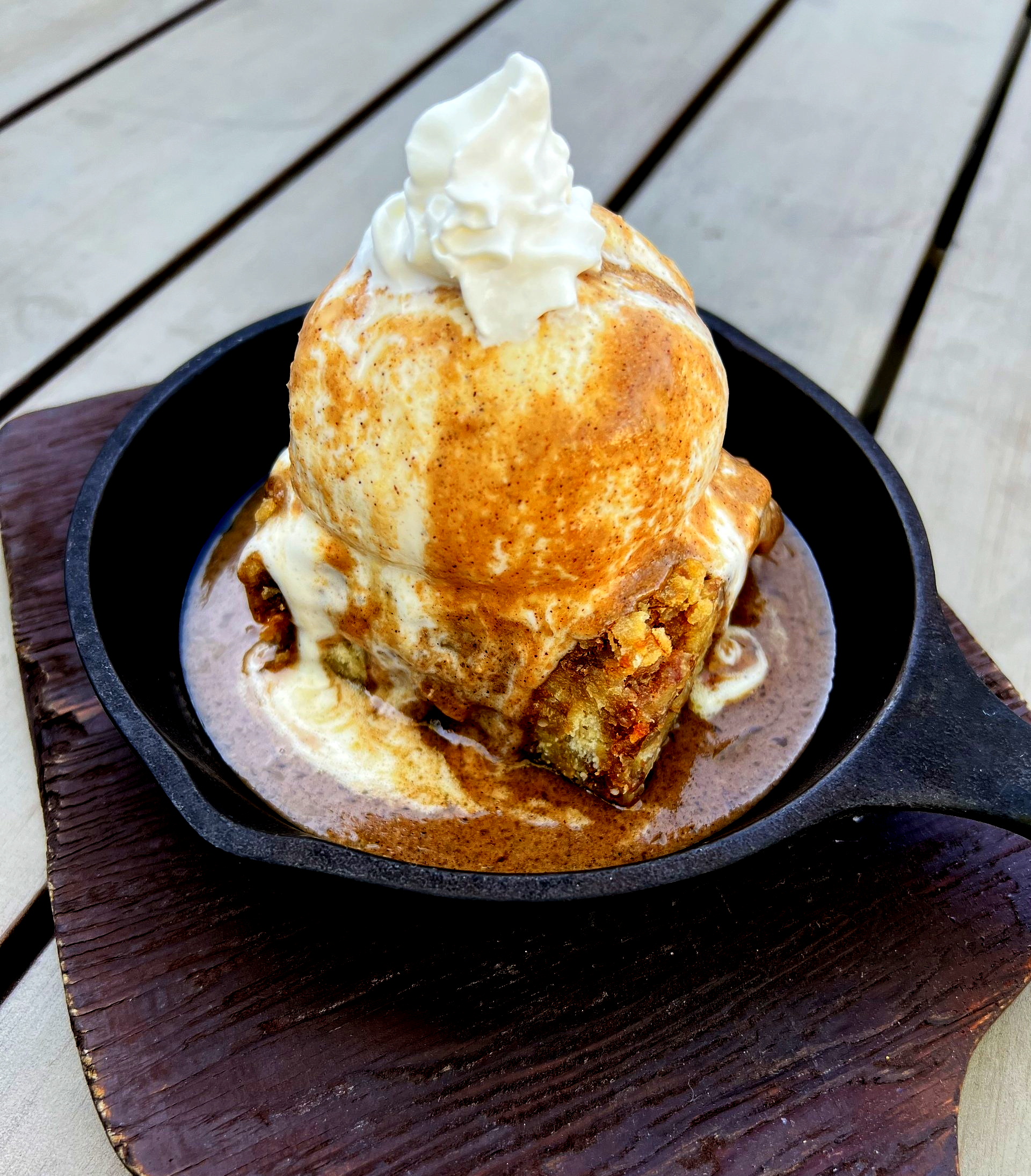 Dessert in skillet: warm bread pudding topped with vanilla ice cream, whipped cream, and cinnamon.