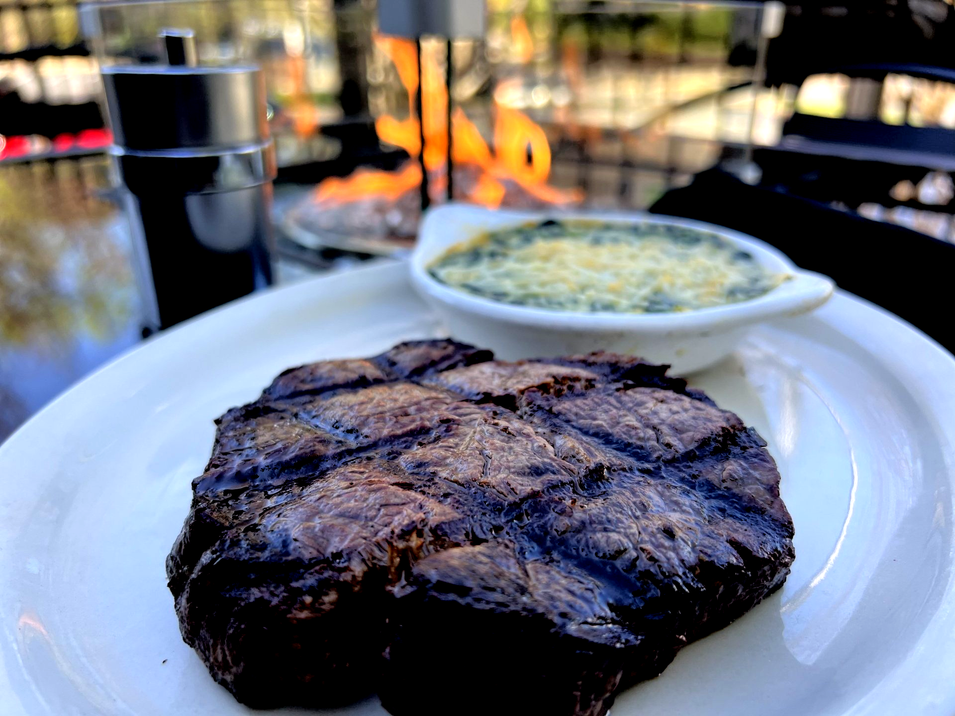 Grilled steak with creamed spinach, salt and pepper grinder, fire in background.