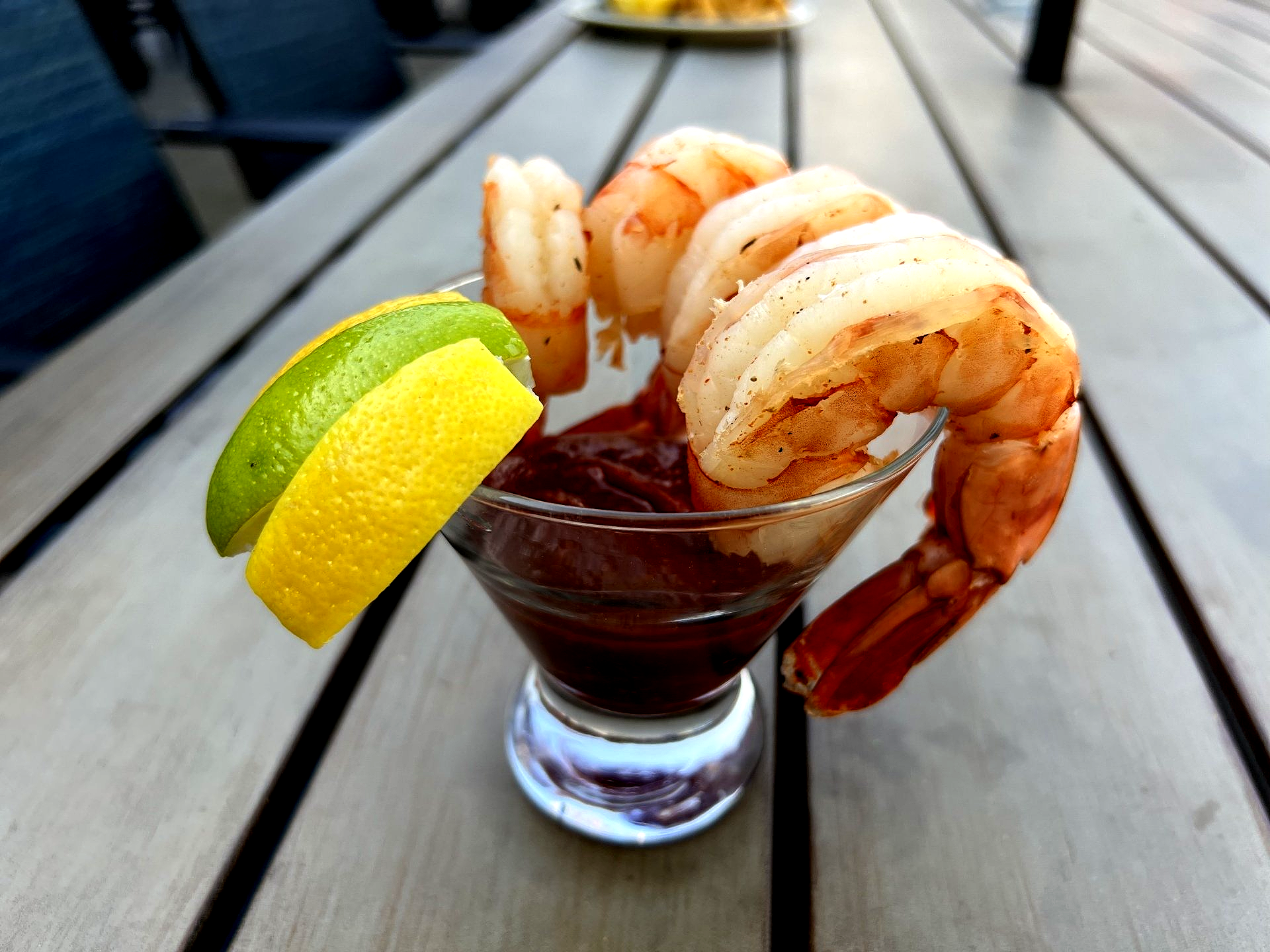 Shrimp cocktail: Large cooked shrimp arranged in a glass with red sauce and lemon/lime wedges, on a wooden table.