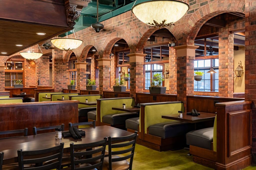 Cozy restaurant interior with brick arches, green booths, wooden tables, and warm hanging lights