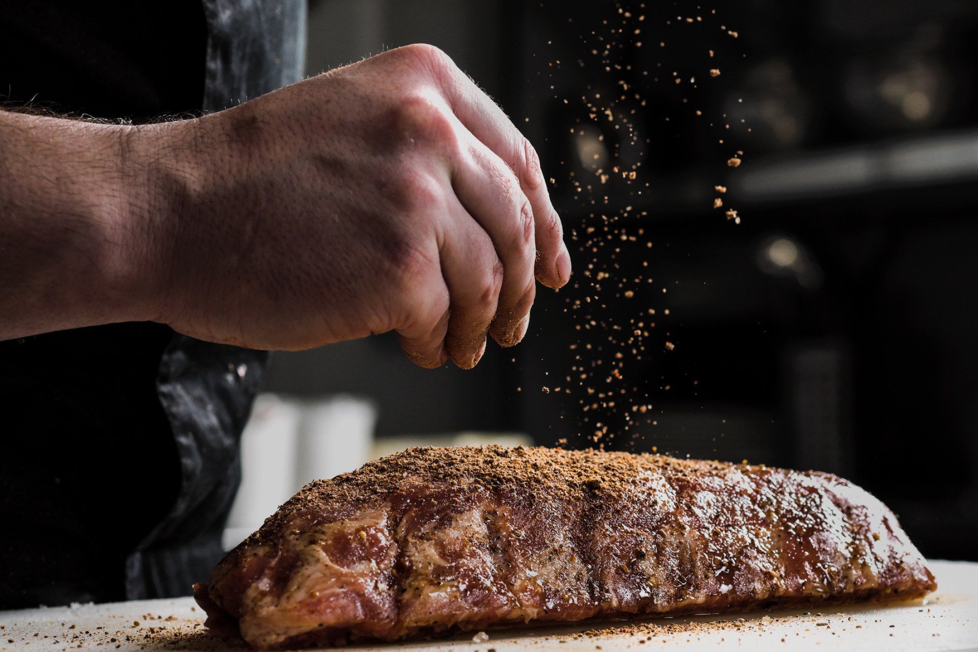 Hand seasoning a rack of ribs with a dry rub on a white cutting board.
