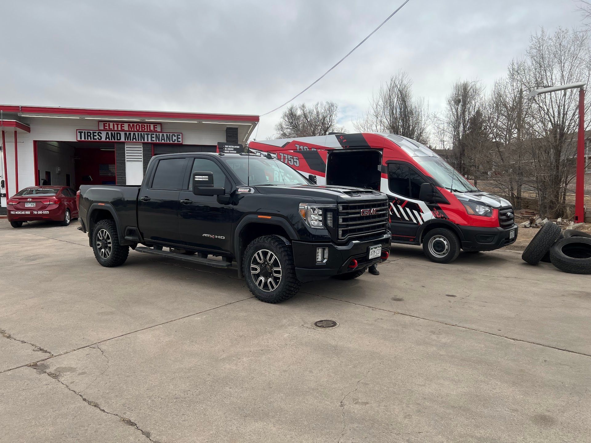 Black truck and van parked outside a tire shop on a cloudy day. | Elite Mobile Tires and Maintenance