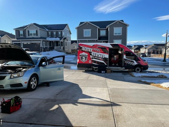 A car being worked on in a driveway, with a mobile service van nearby, in a residential area. | Elite Mobile Tires and Maintenance