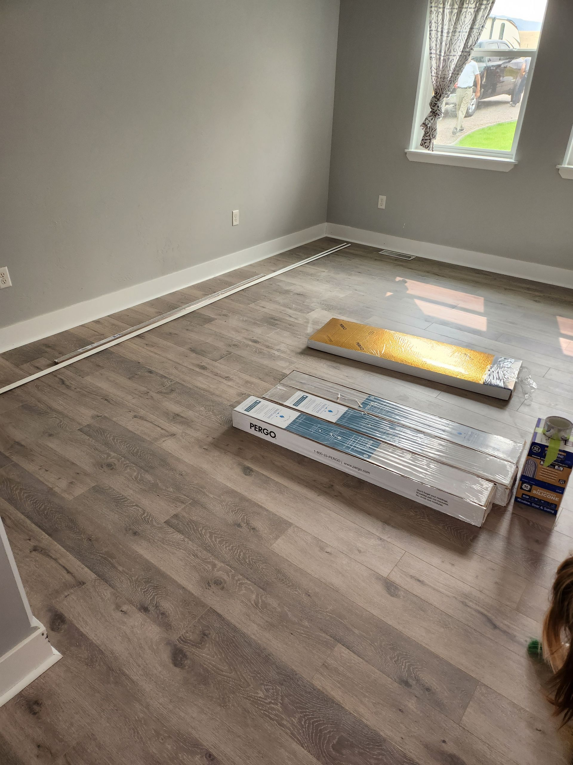 Room with new grey flooring, white trim, two boxes of flooring, near window.