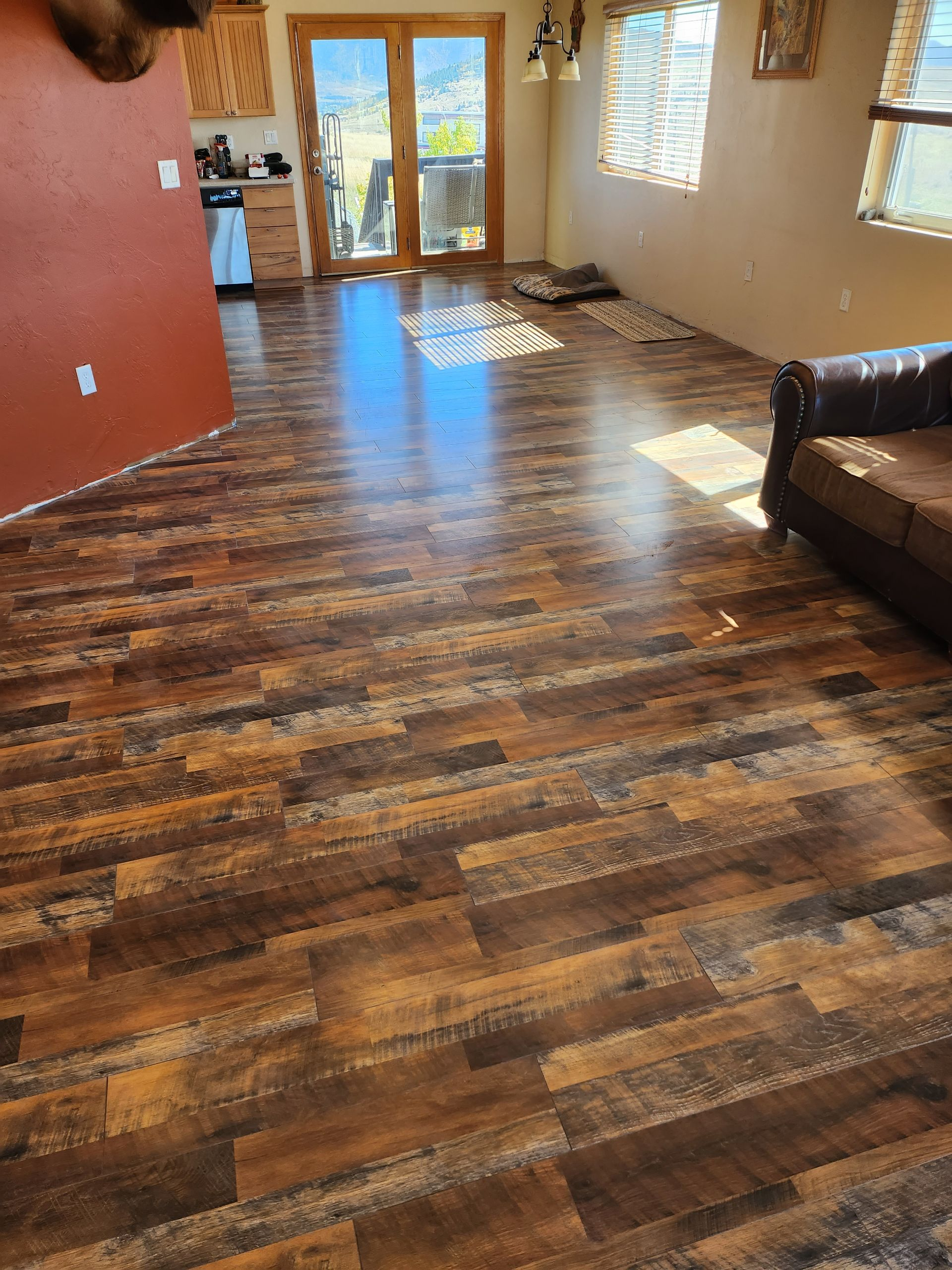 Wood-look laminate flooring in a living room, with a dark brown and tan color scheme. Sun beams through the windows.