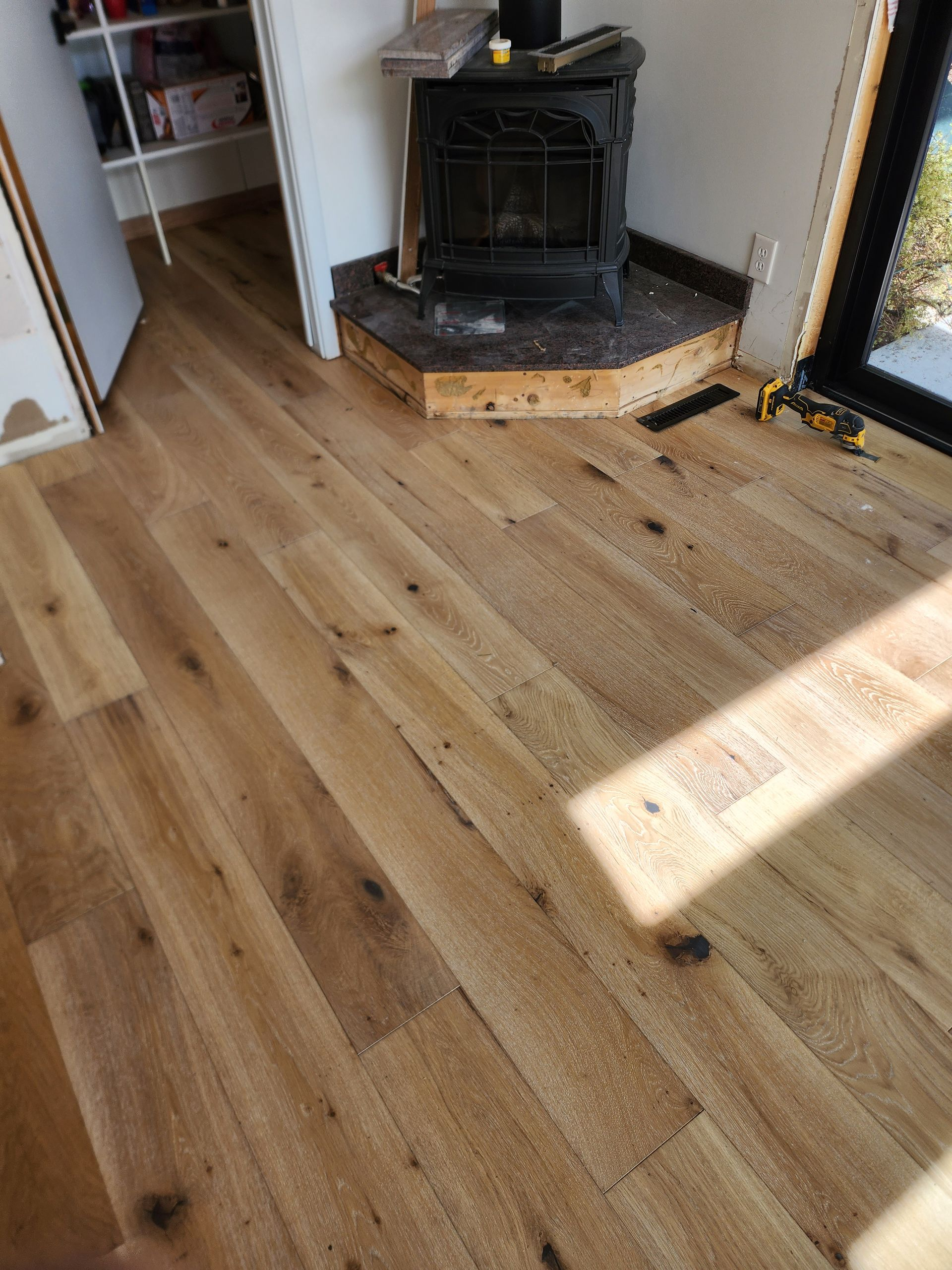 Hardwood flooring installed around a wood-burning stove, unfinished trim visible.