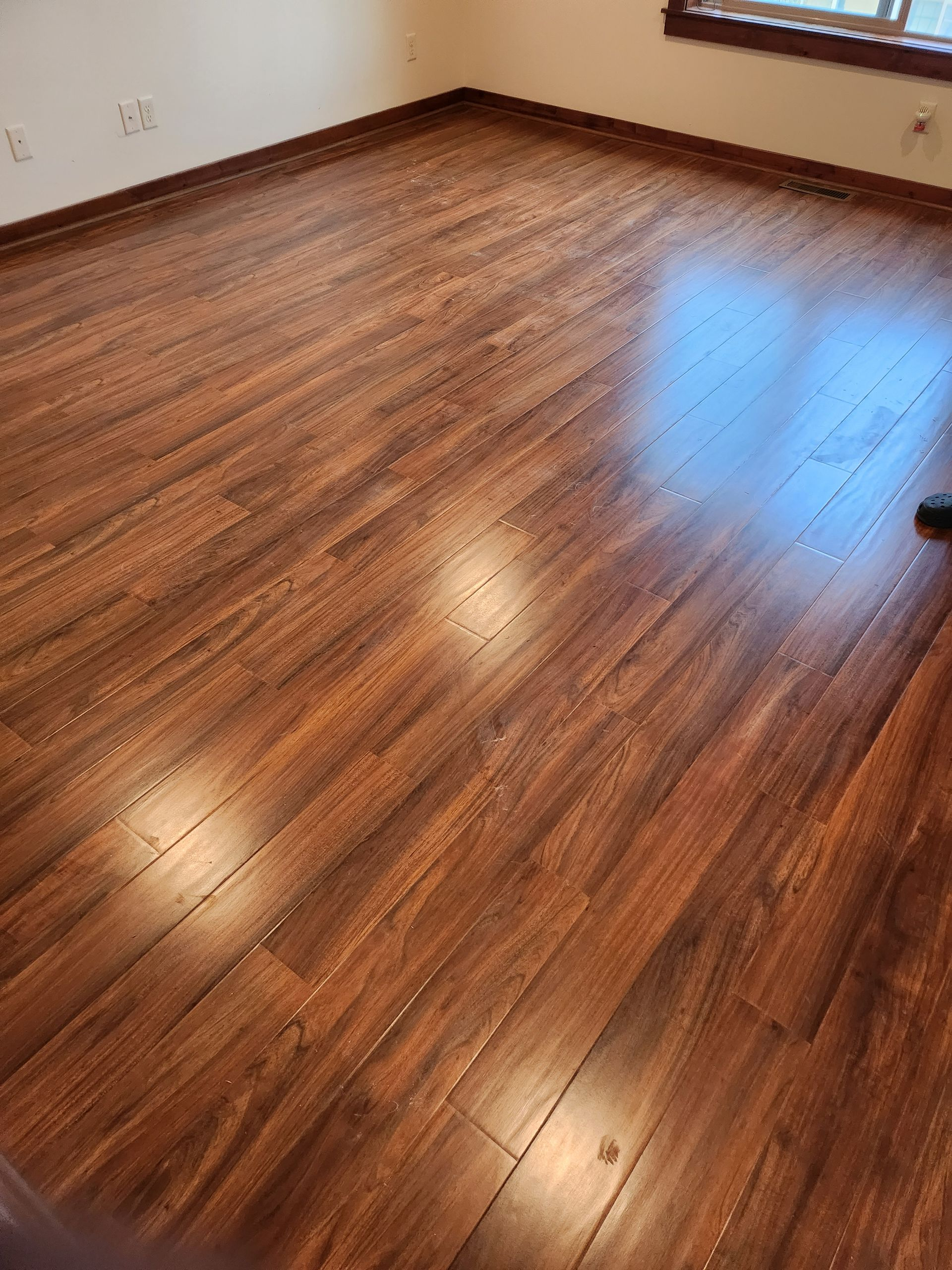 Brown wooden laminate flooring in a room with a window, reflecting light.