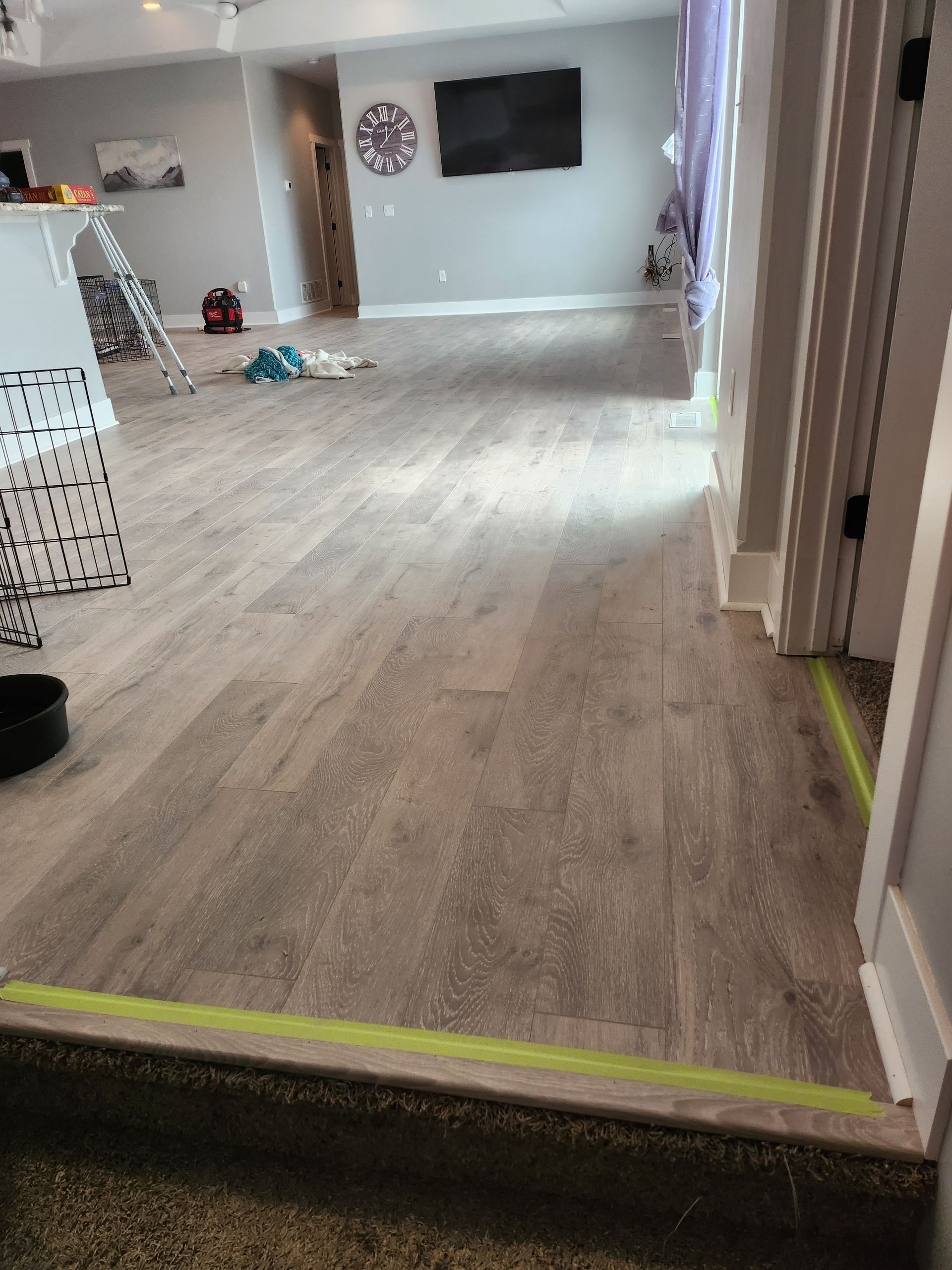 New wood flooring installation in a room, light brown planks. Doorway with green tape.