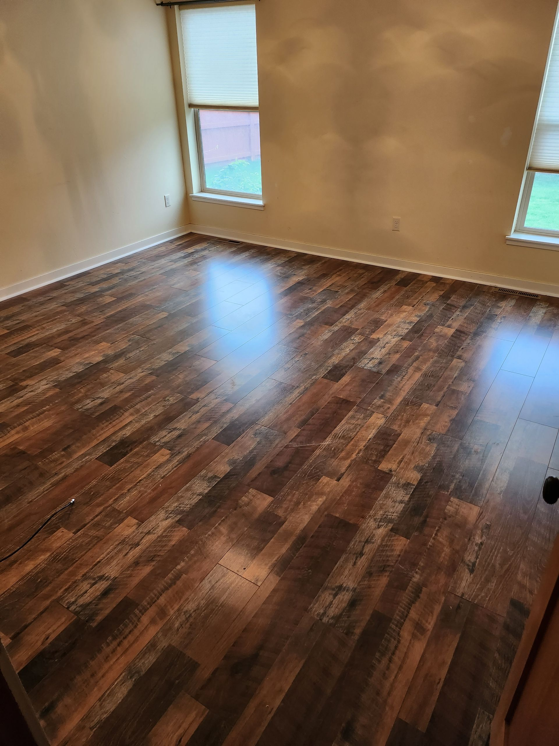 Dark wood-look flooring in a room with two windows and tan walls.