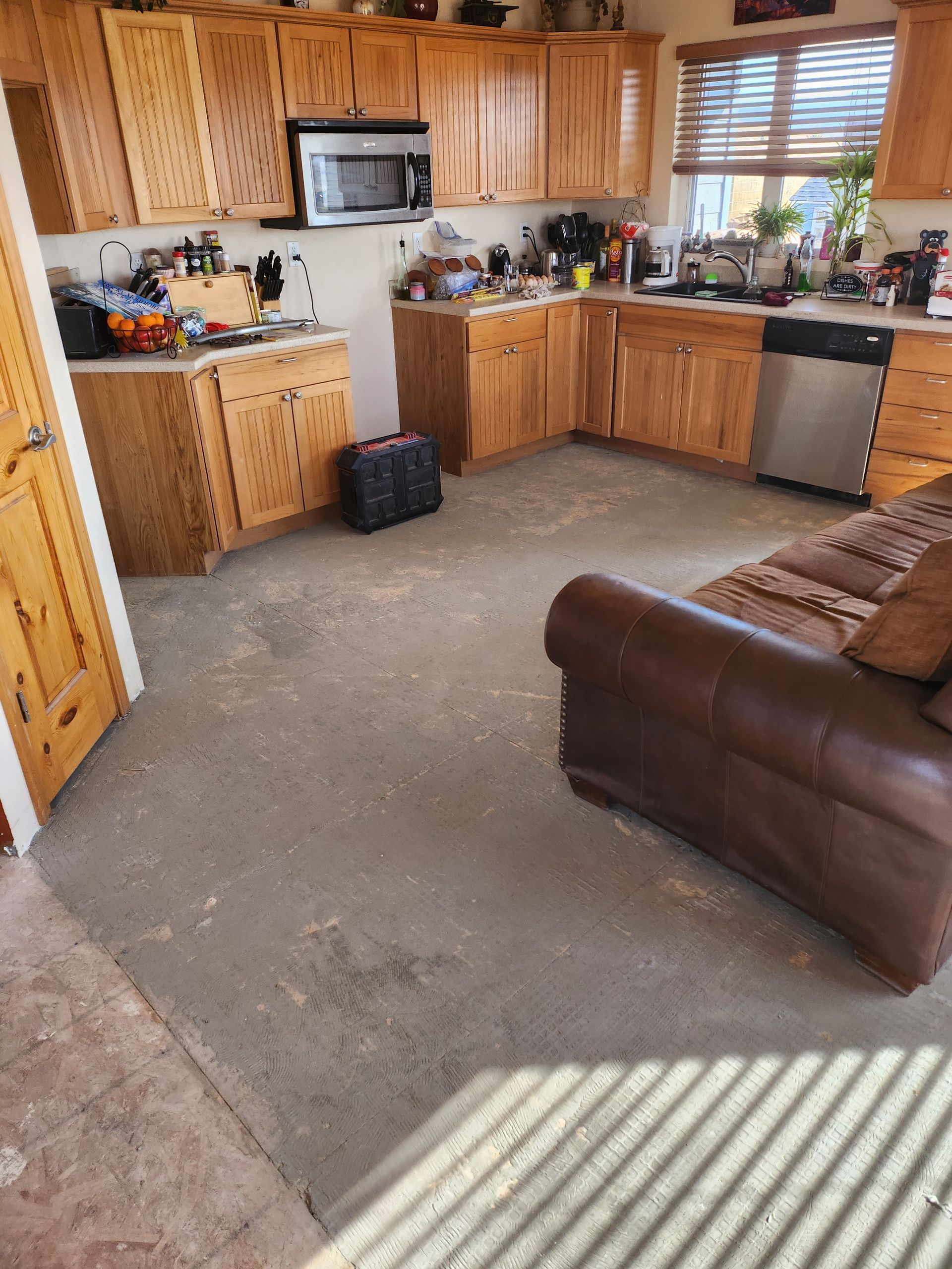 Kitchen with wood cabinets, microwave, and stainless steel appliances. Concrete floor, brown leather couch.