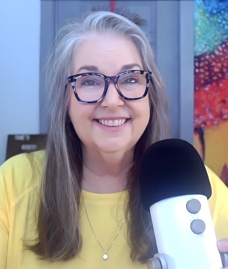 Smiling speaker in glasses at a microphone, wearing a yellow top in a colorful studio