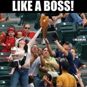 Woman catches baseball with one hand, holding a baby in the other, crowd reaching.