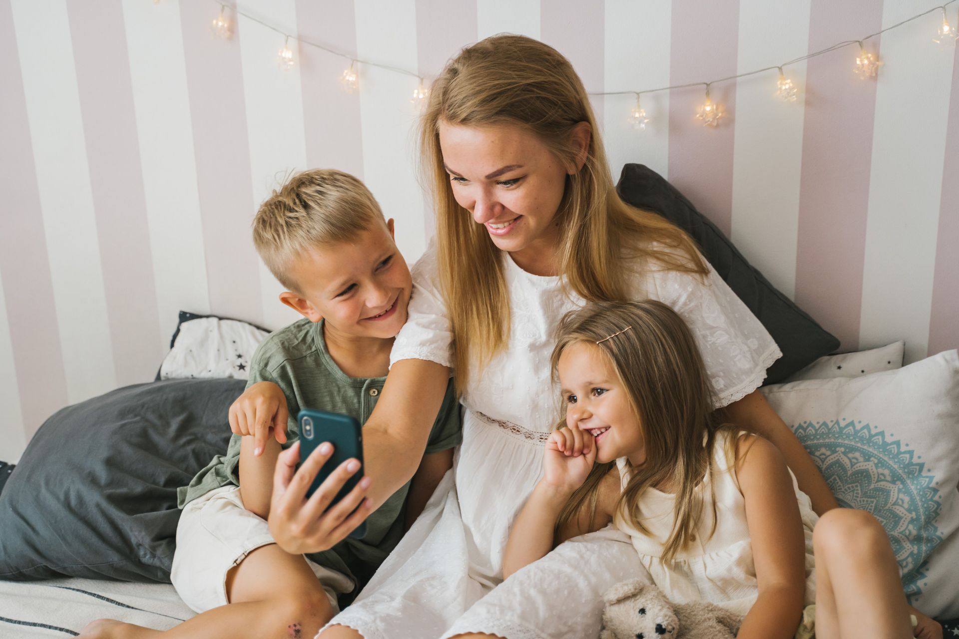 Family reading together on a bed, smiling under warm string lights