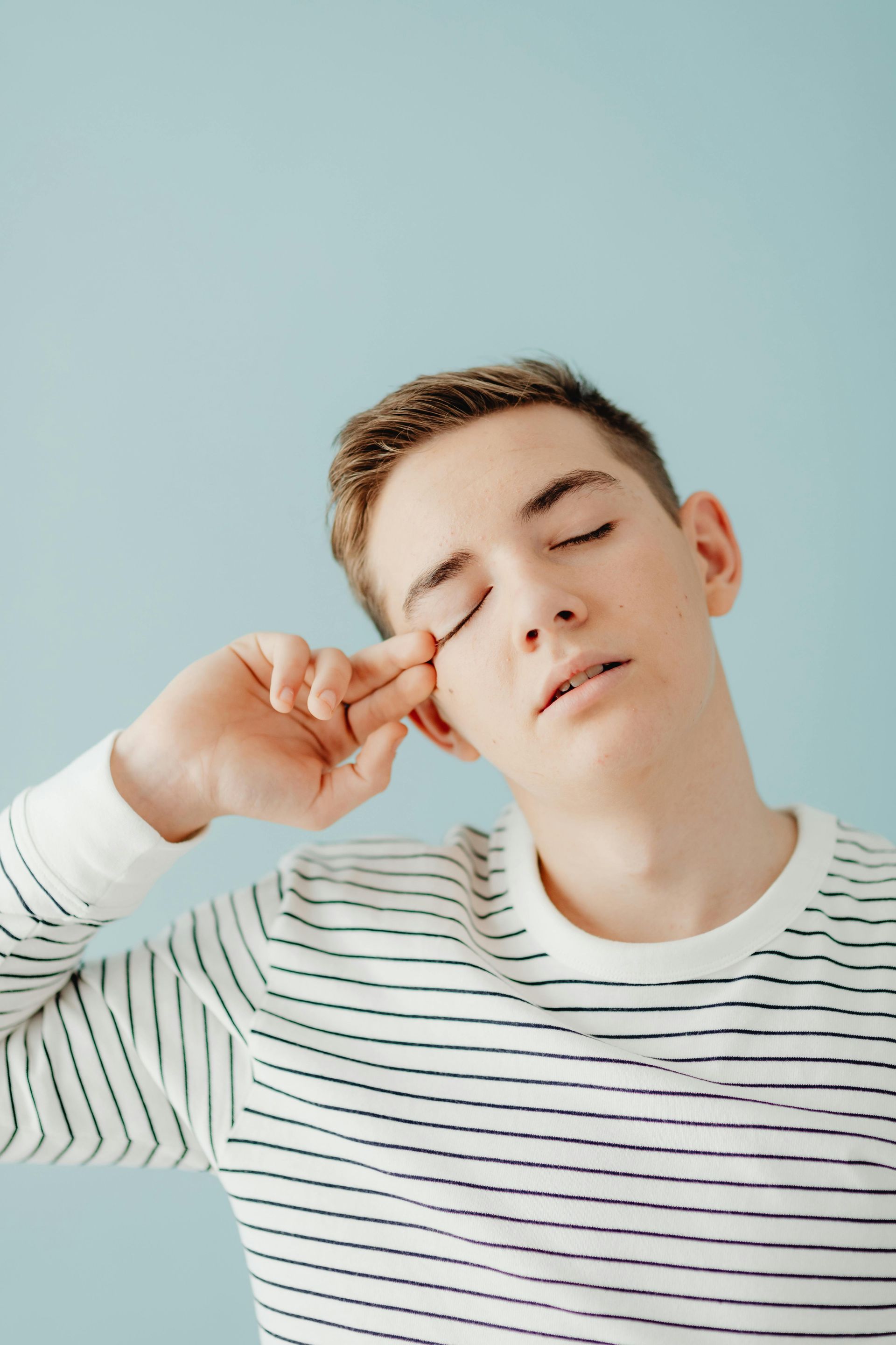 Person in a white striped shirt resting their head on a hand against a light blue background