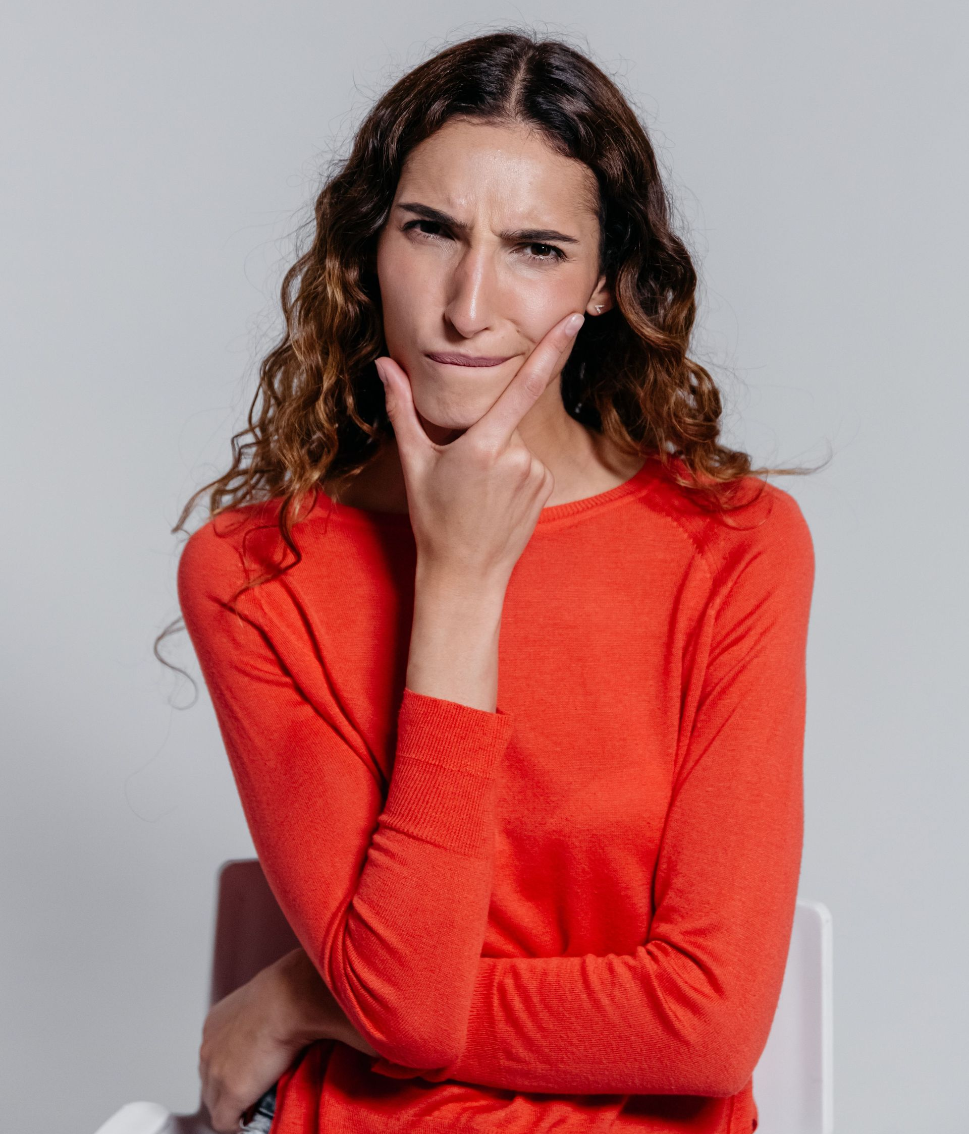 Woman in a red sweater resting her chin on her hand, looking thoughtfully at the camera.