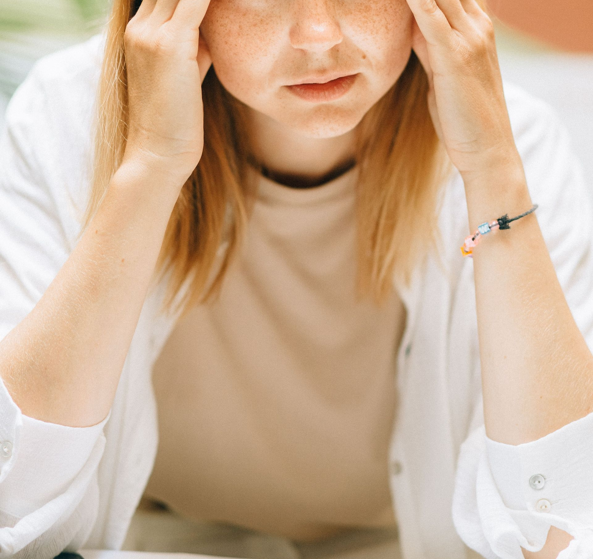 Person holding their head with eyes closed, wearing a beige top and white cardigan, looking stressed.