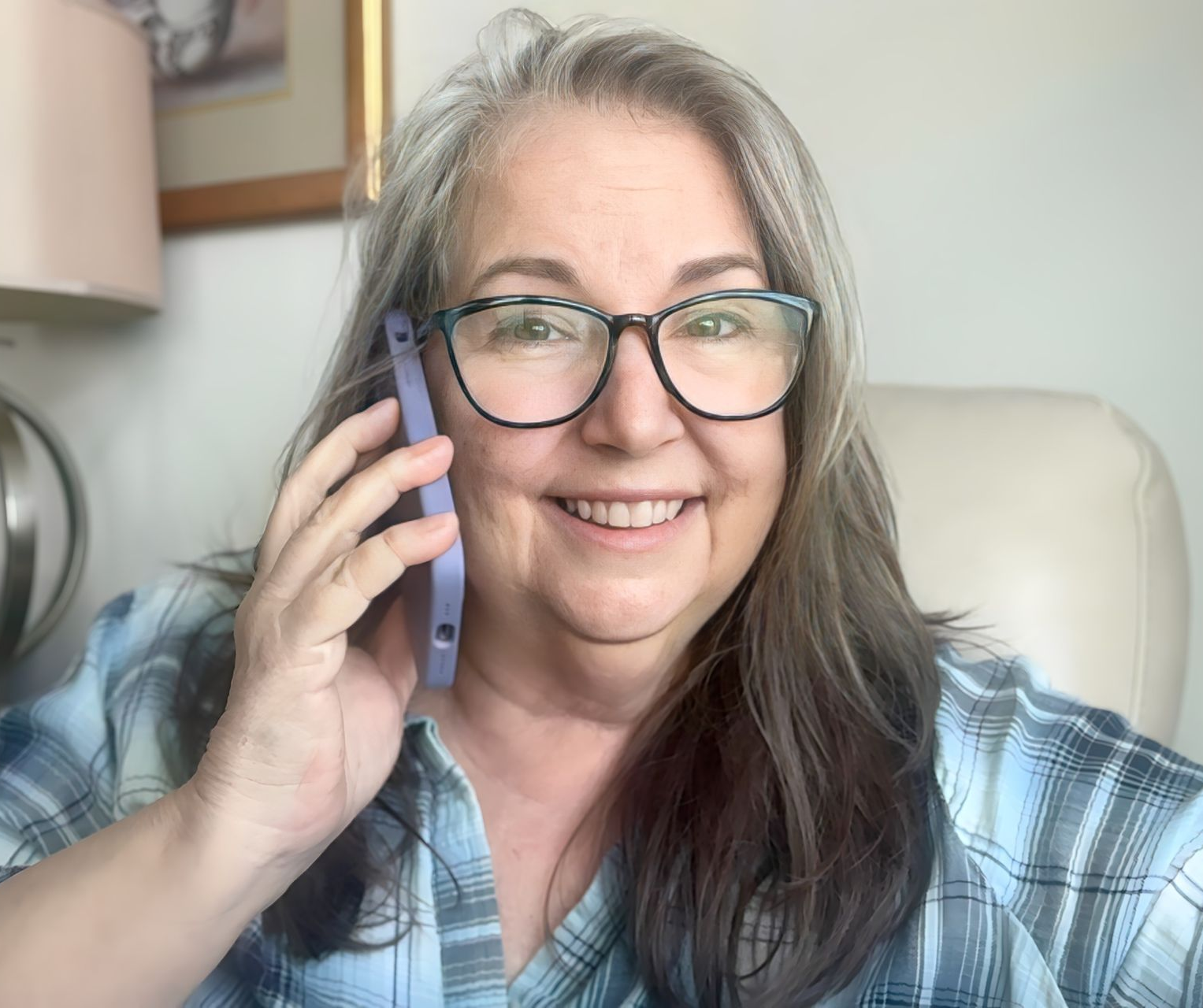 Smiling person with glasses holding a phone to their ear on a couch