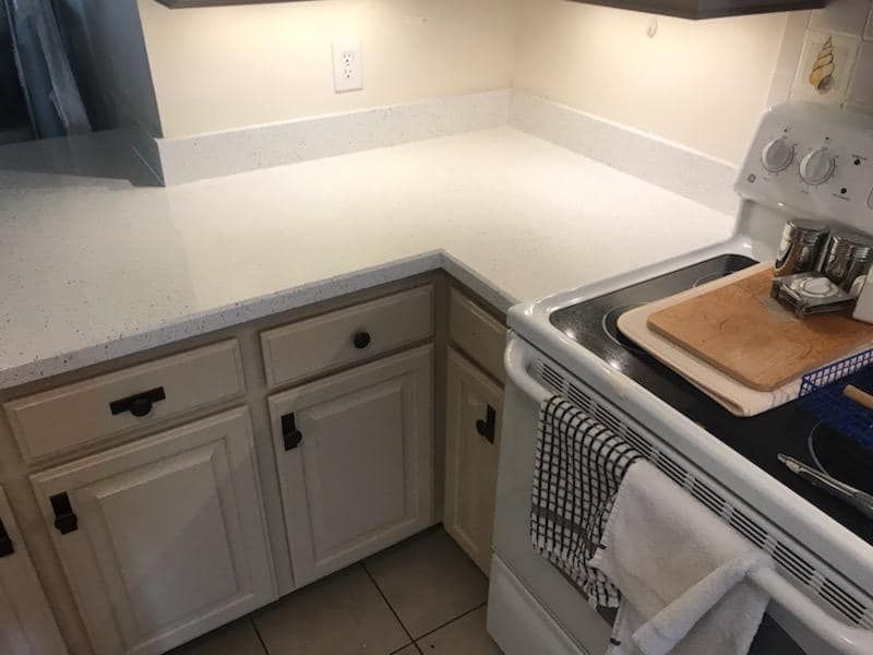 Kitchen corner featuring light cabinets with dark handles, white speckled countertops, and an electric stove.