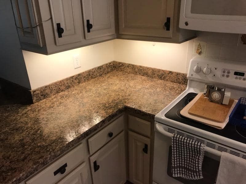 Kitchen counter with brown granite-style laminate, white cabinets with black knobs, and under-cabinet lighting.