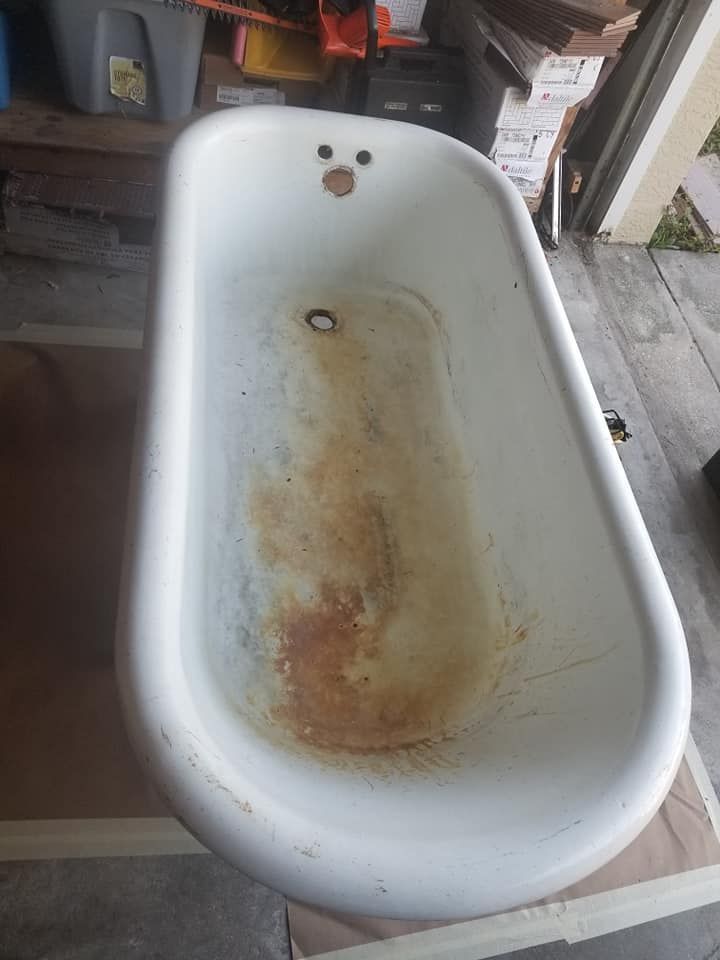 A white, vintage clawfoot-style bathtub sits in a cluttered garage with visible rust staining on the interior basin.