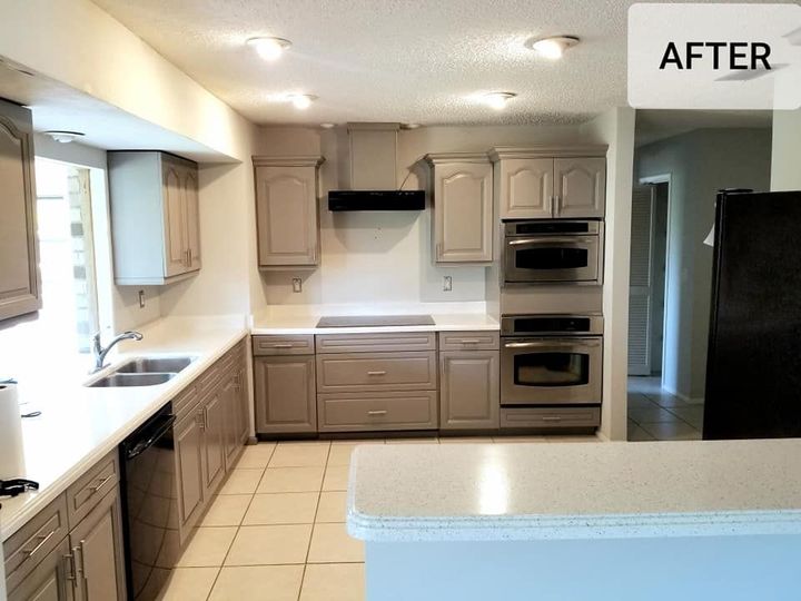 Modern kitchen with grey cabinets, light countertops, stainless steel wall ovens, and black appliances.