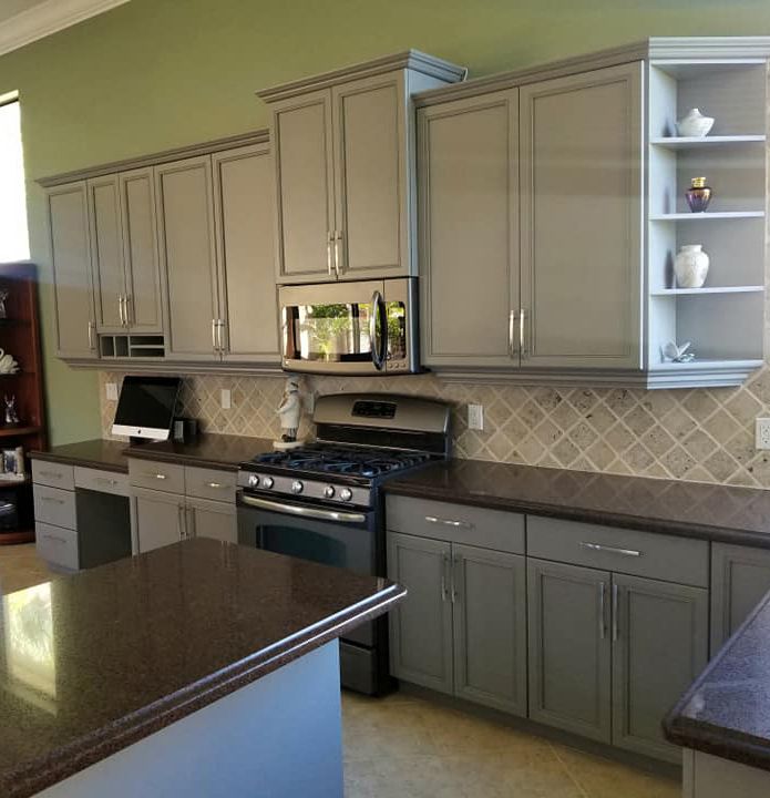A kitchen featuring grey cabinets, a dark countertop, a gas range with an overhead microwave, and a tiled backsplash.