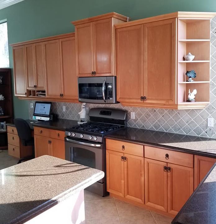 A kitchen with light wood cabinets, dark granite countertops, stainless steel appliances, and a home office workstation.