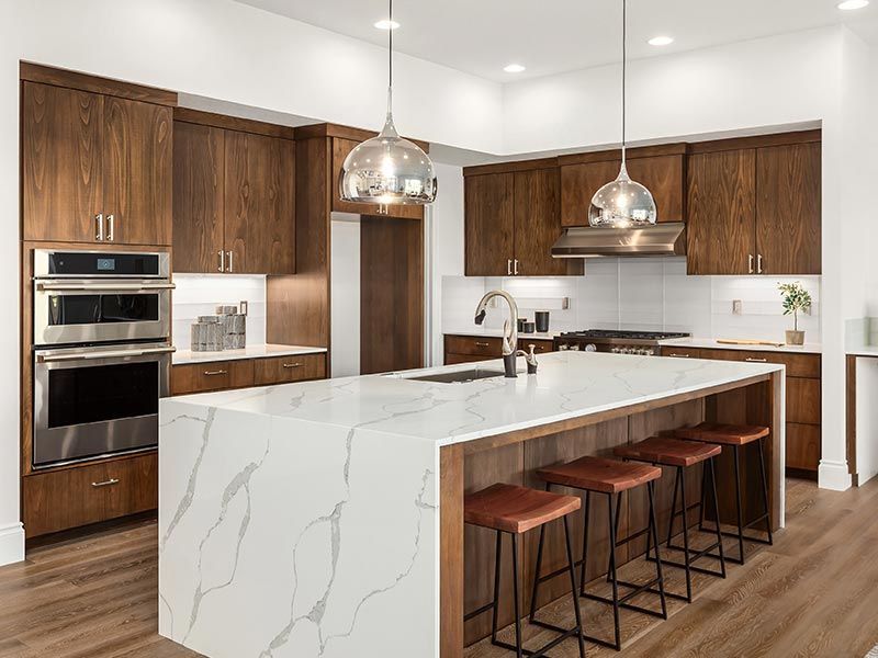 A modern kitchen with dark wood cabinets, a large white marble-topped island, and four stools on a hardwood floor.