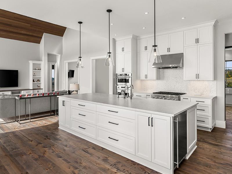A bright kitchen features a large white island, white cabinetry, stainless steel appliances, and dark hardwood floors.