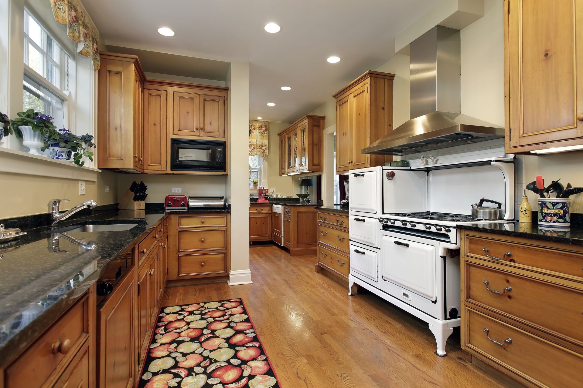 A spacious kitchen with natural wood cabinets, granite countertops, a large white stove, and a colorful patterned rug.
