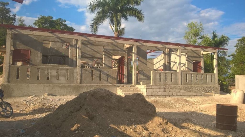 A partially constructed building with unfinished concrete walls and a red metal roof sits under a blue sky.
