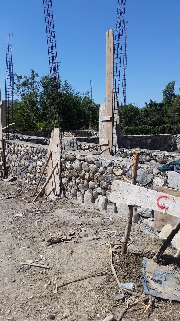A construction site with stone walls and wooden supports, featuring exposed rebar columns
