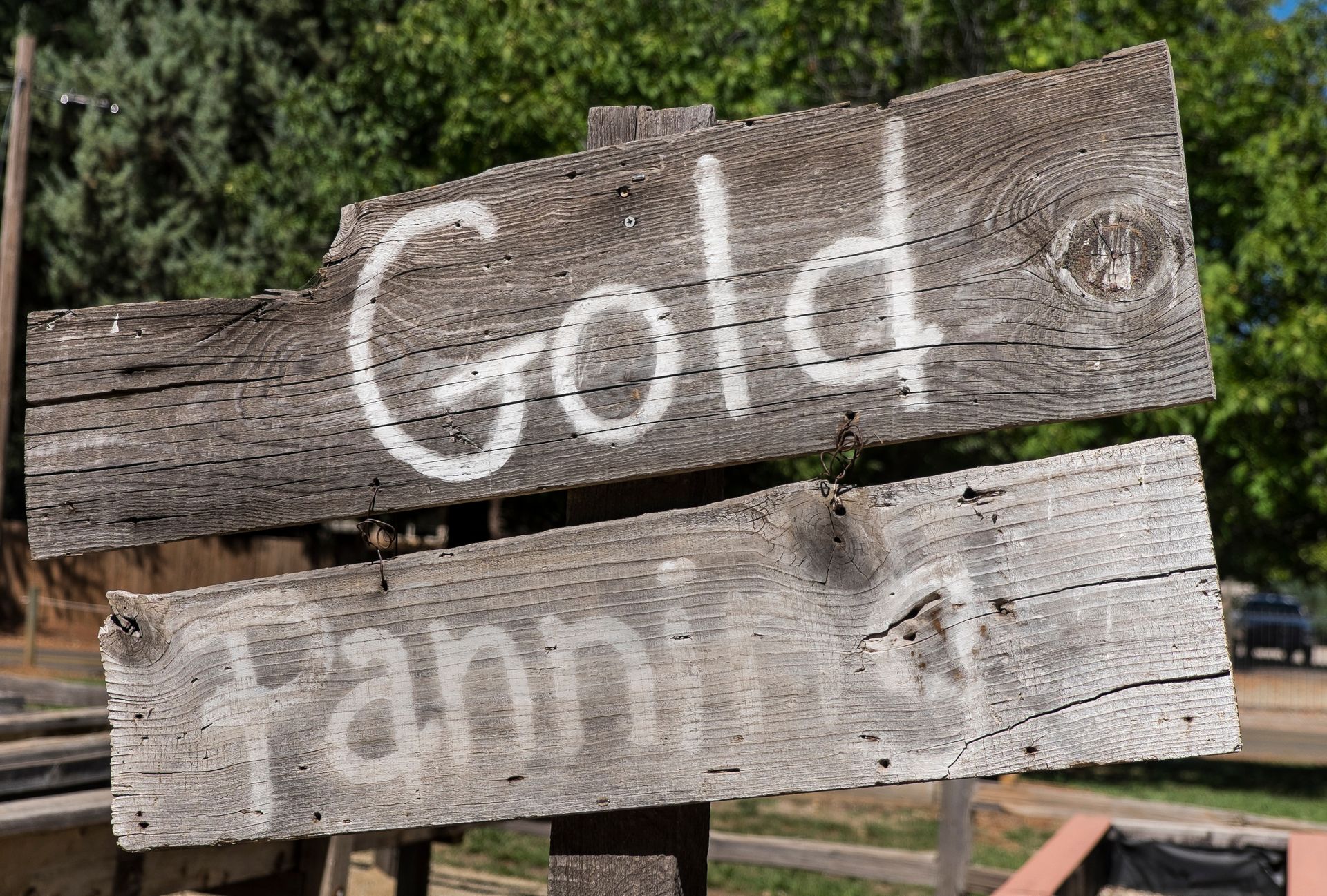 Weathered wooden sign reading “Gold Pan #1” in white paint, outdoors with trees in background