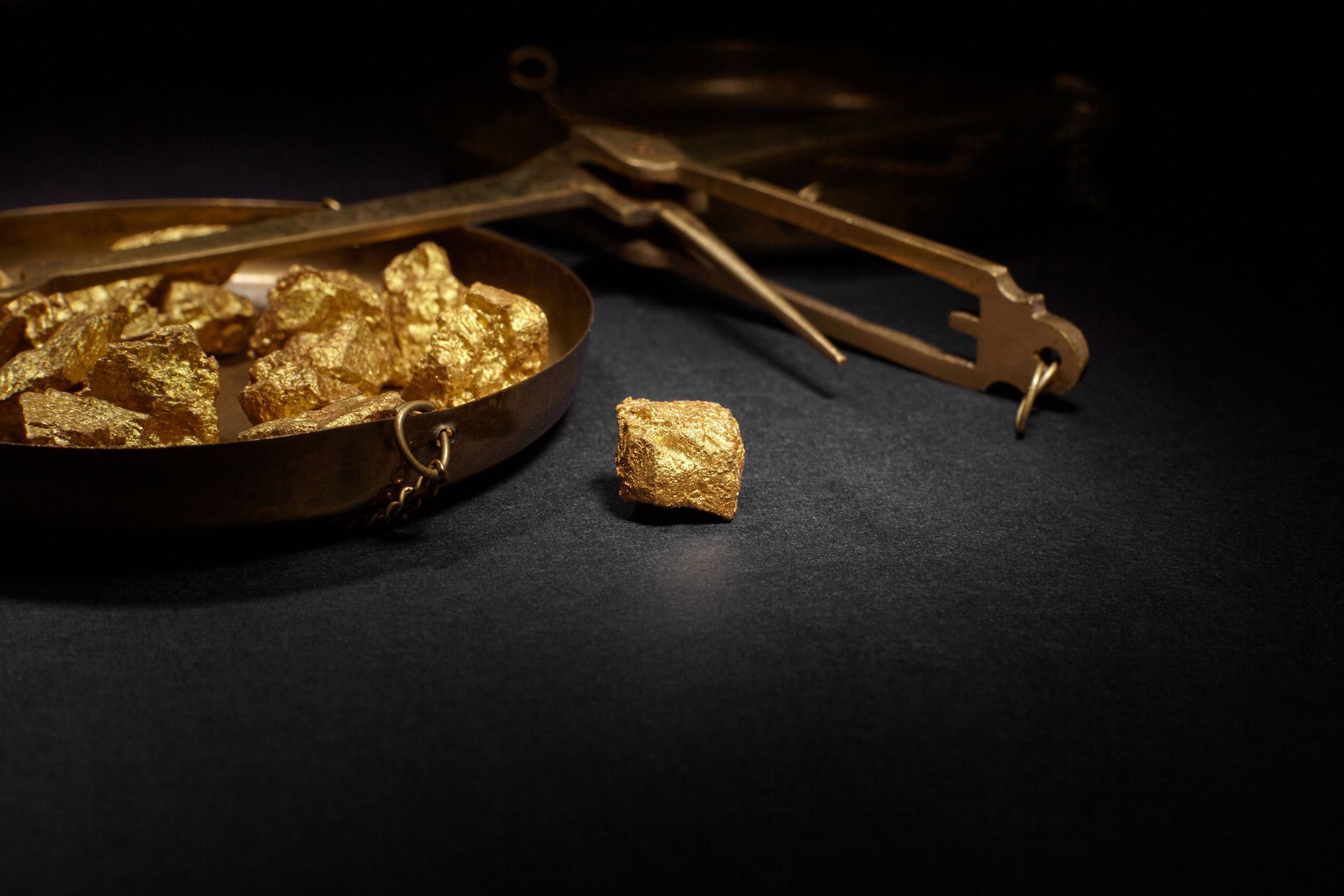 Gold nuggets in a shallow bowl beside a pan and tweezers on a dark surface