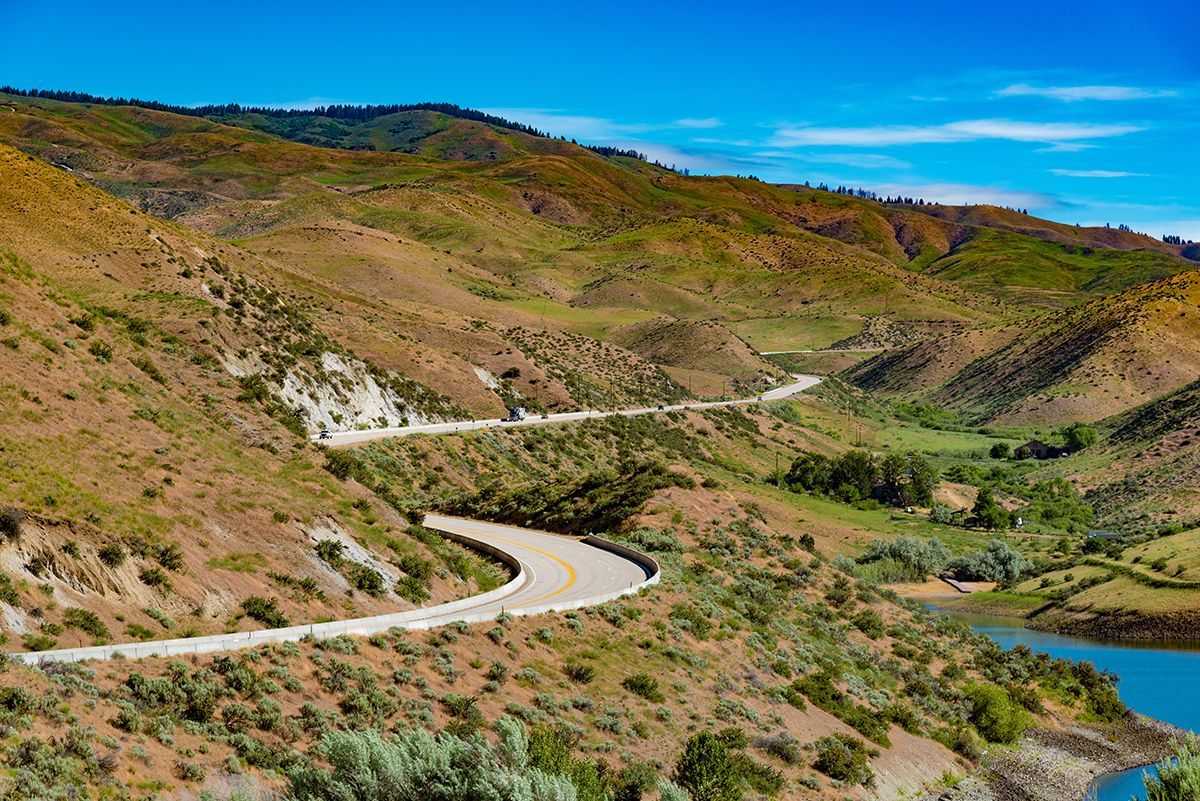A winding road in the middle of a valley with a lake in the background.