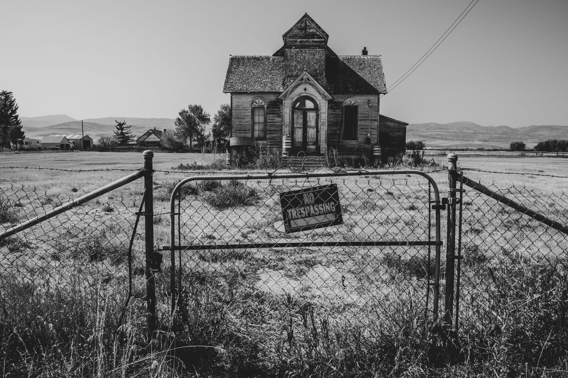 Abandoned house behind a chain link fence in a field;