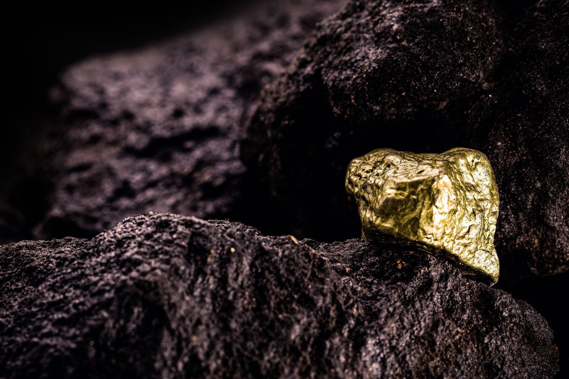 Gold nugget nestled among dark rocks in dim light