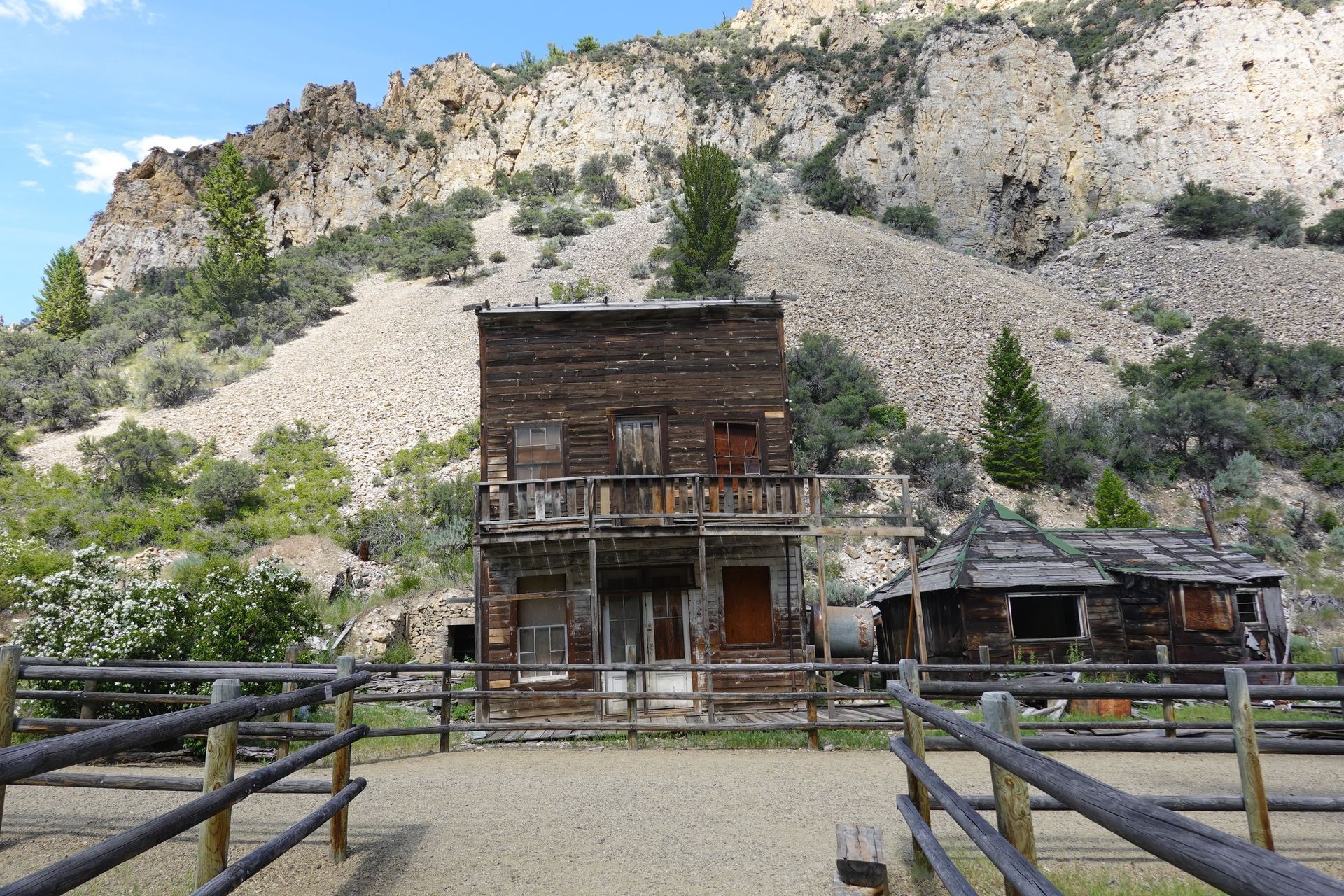 Weathered wooden buildings in a fenced enclosure, with a mountain backdrop under a cloudy sky.