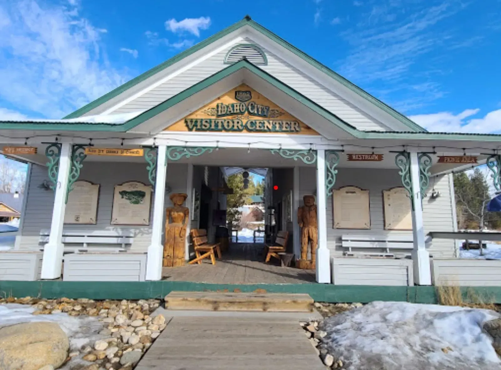Visitor center entrance with snow, wooden carvings, and signs under a green-trimmed roof.
