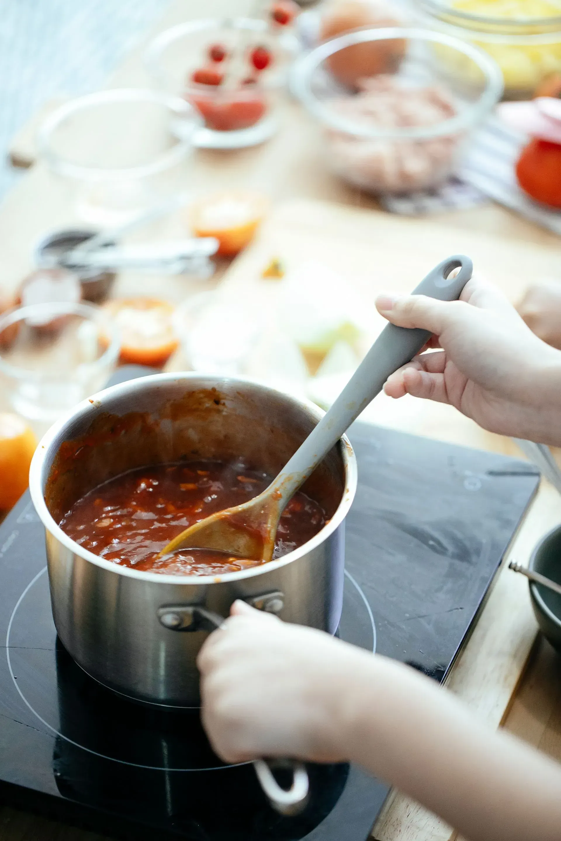 A person is stirring a pot of sauce with a spoon.