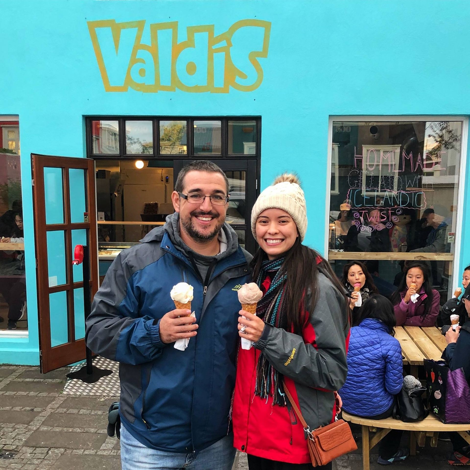A couple smiles, holding ice cream cones in front of a blue Valdi's ice cream shop.