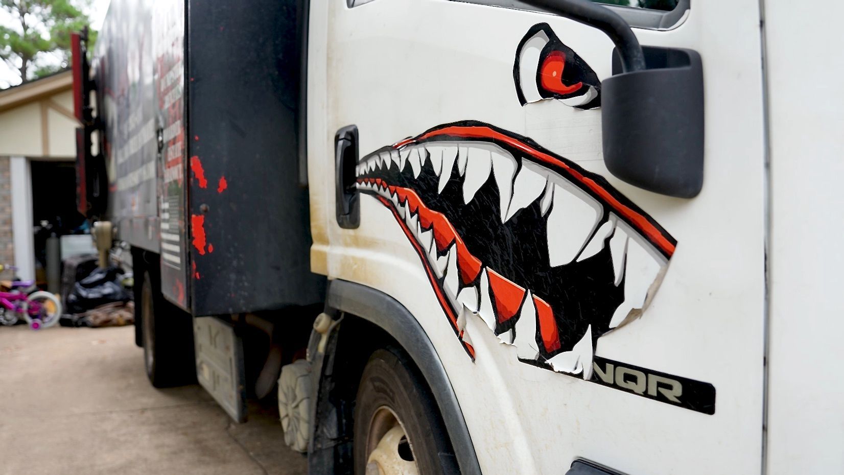 White truck with shark-mouth decal on the side. Black and red accents.