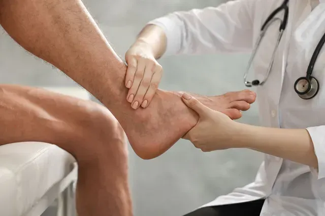 Doctor examining a patient's ankle. Doctor wears a white coat and stethoscope.