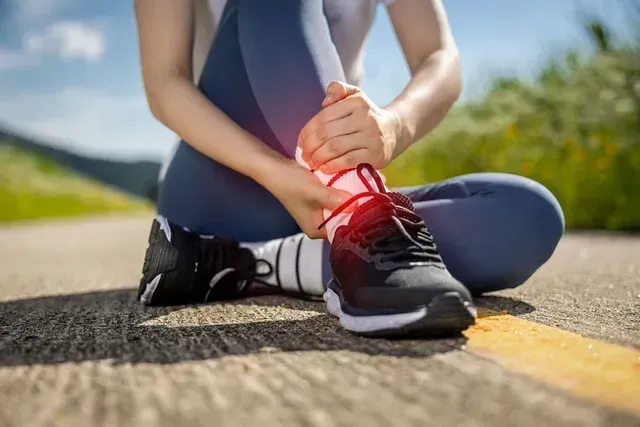 Woman sitting on road, holding her ankle. Red highlights show the injured area.