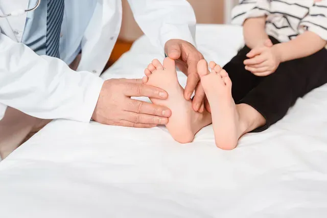 Doctor examining a child's feet on a white medical table.