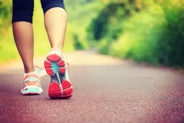 Person walking on a red path in a park, wearing sneakers and athletic wear.