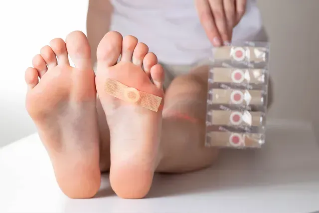 Person with feet, one foot with a bandage, holding wart removal pads.
