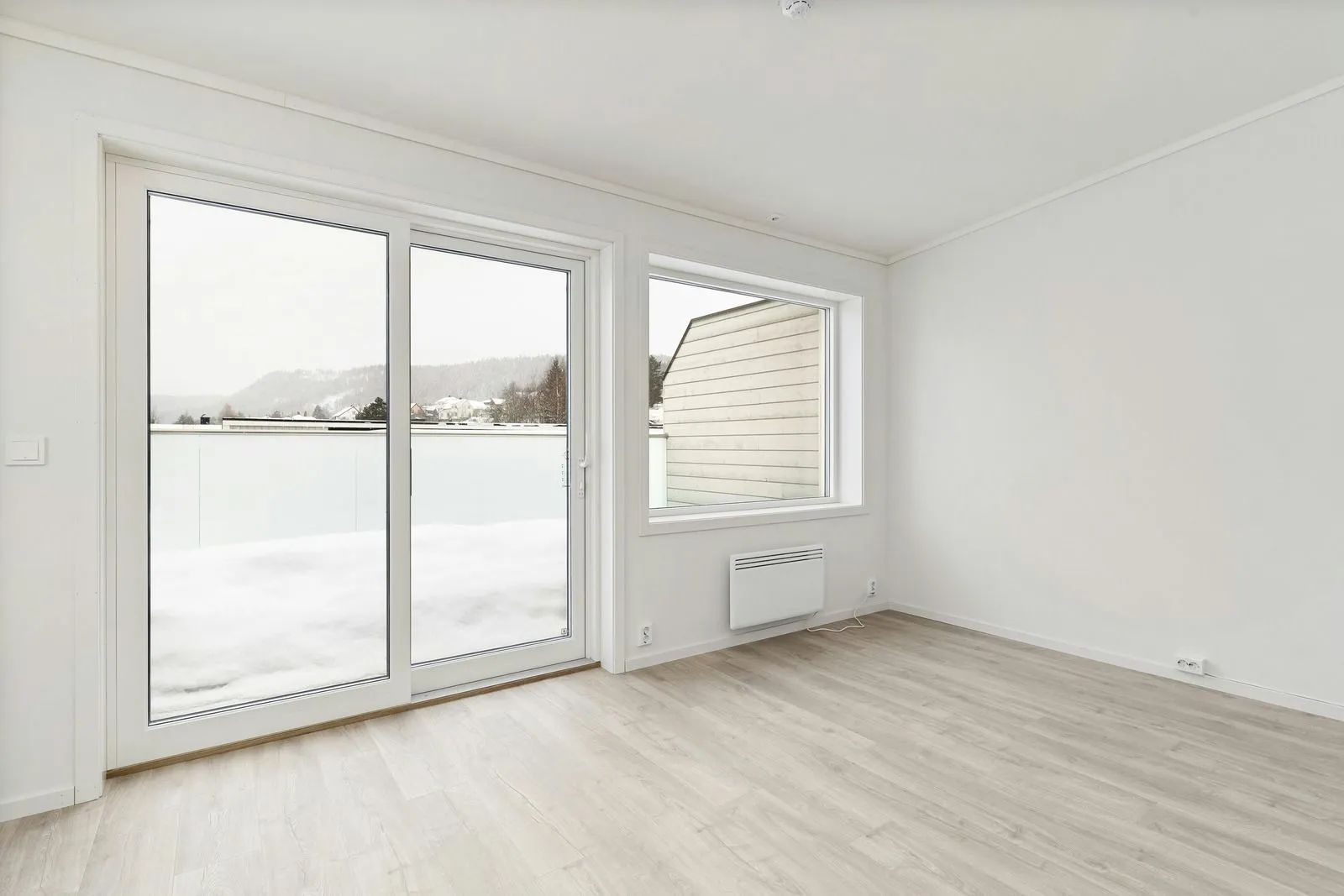 Empty white room with large windows, light wood floor, and scenic outdoor view.