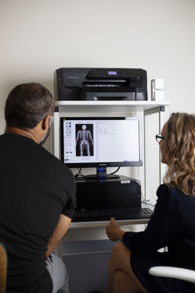Two people reviewing an X-ray on a computer screen in a medical setting. A printer sits above the monitor.