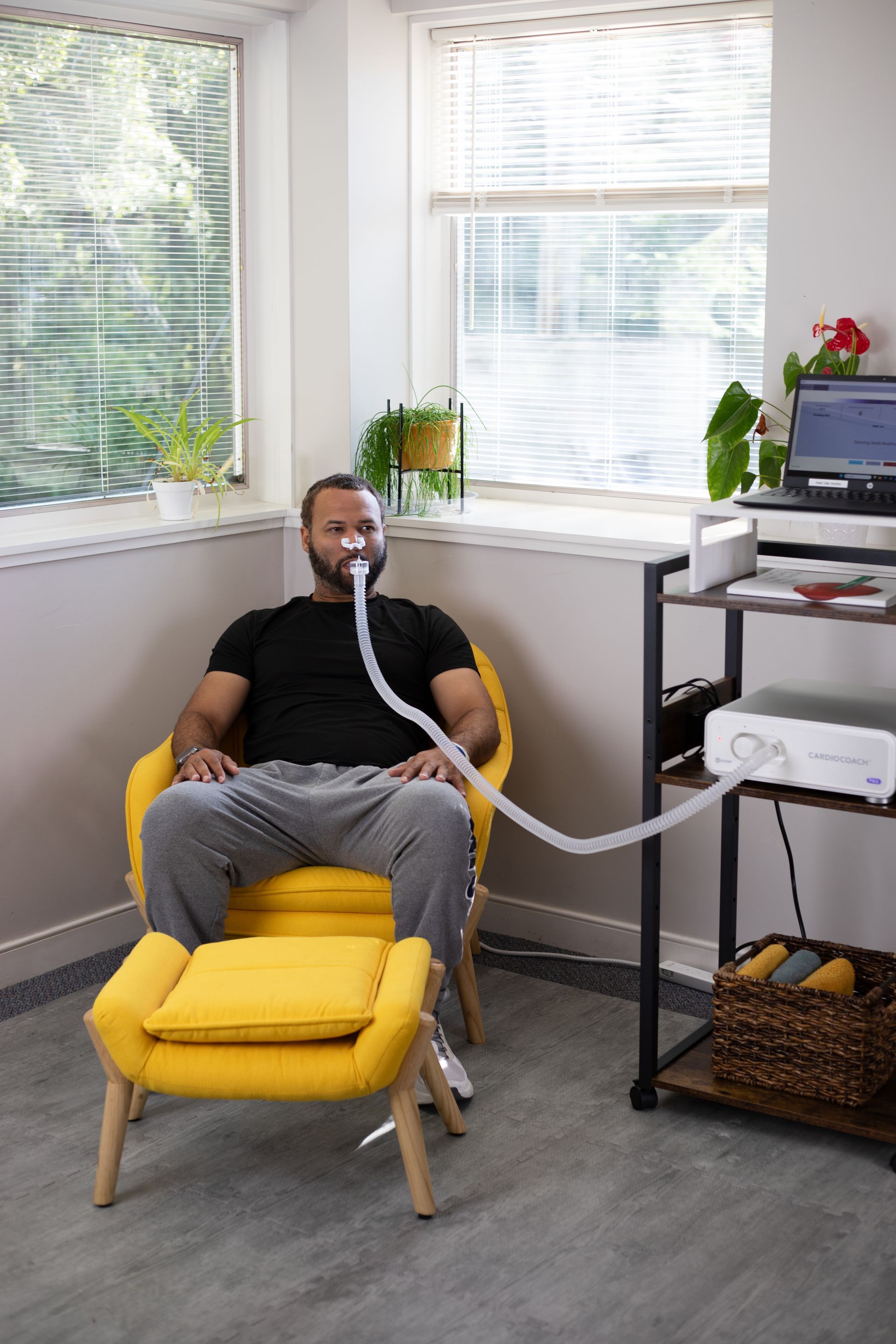 Man seated in yellow chair with a breathing tube, medical testing equipment nearby.
